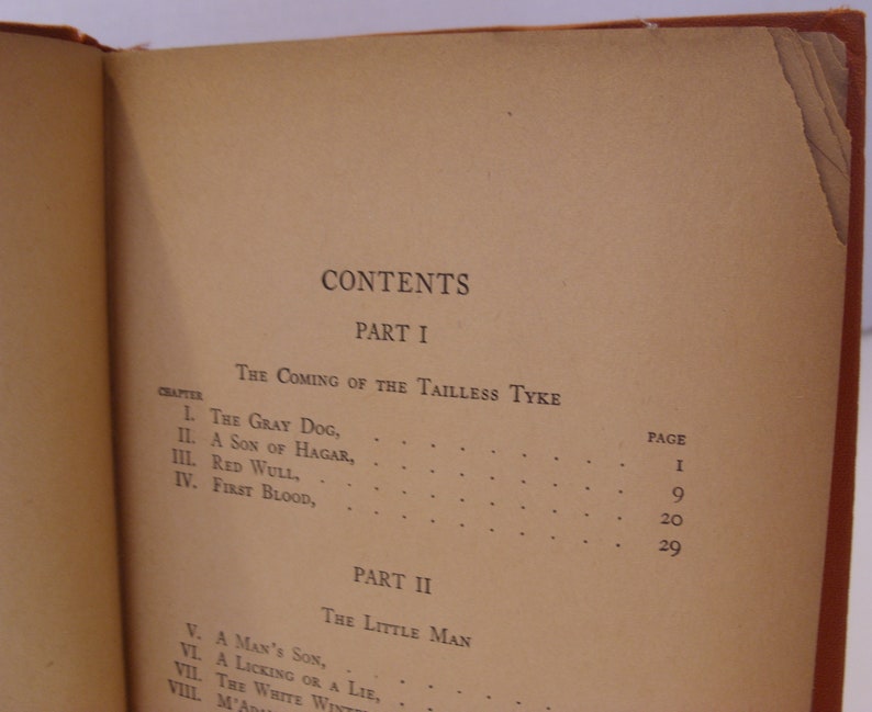 May include: A book with a brown cover and a table of contents for a novel titled "The Coming of the Tailless Tyke" and "The Little Man". The table of contents lists the chapters and page numbers.