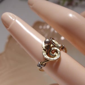 May include: A ring crafted from gold-toned and silver-toned wire, featuring a central spiral design accented with a small metallic sphere. The band is constructed from twisted wire segments, showcasing a mixed-metal aesthetic with a polished finish.