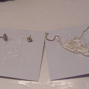 May include: Two silver earrings and a silver chain necklace on white card stock.