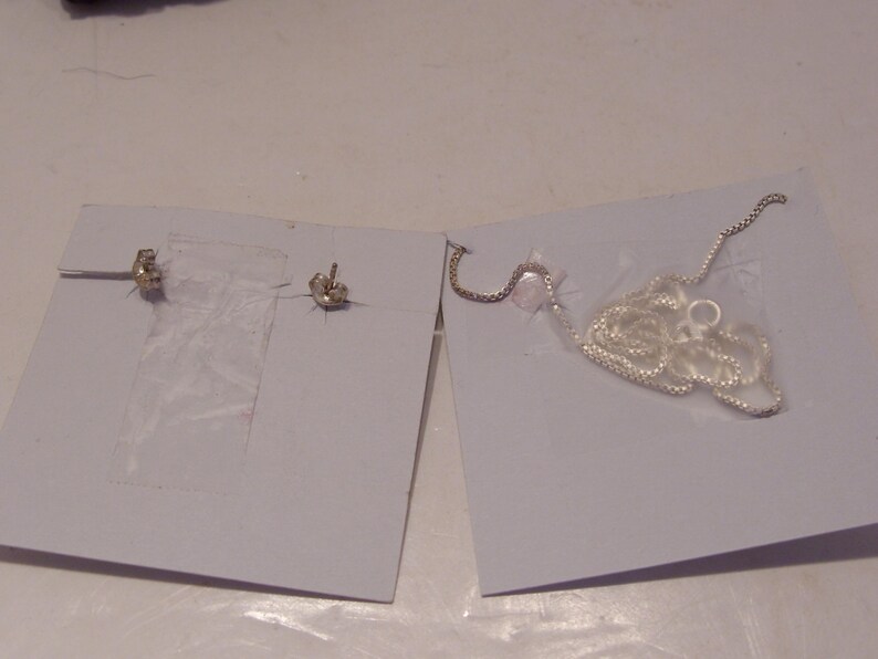 May include: Two silver earrings and a silver chain necklace on white card stock.