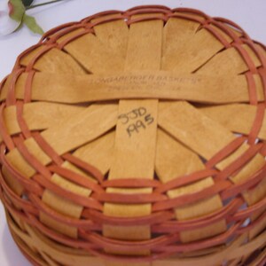May include: A woven basket with a brown and red pattern. The bottom of the basket has a label that reads "Longaberger Basket Co.  744  330-672-1314" and the number "33D A95" is written in black marker.