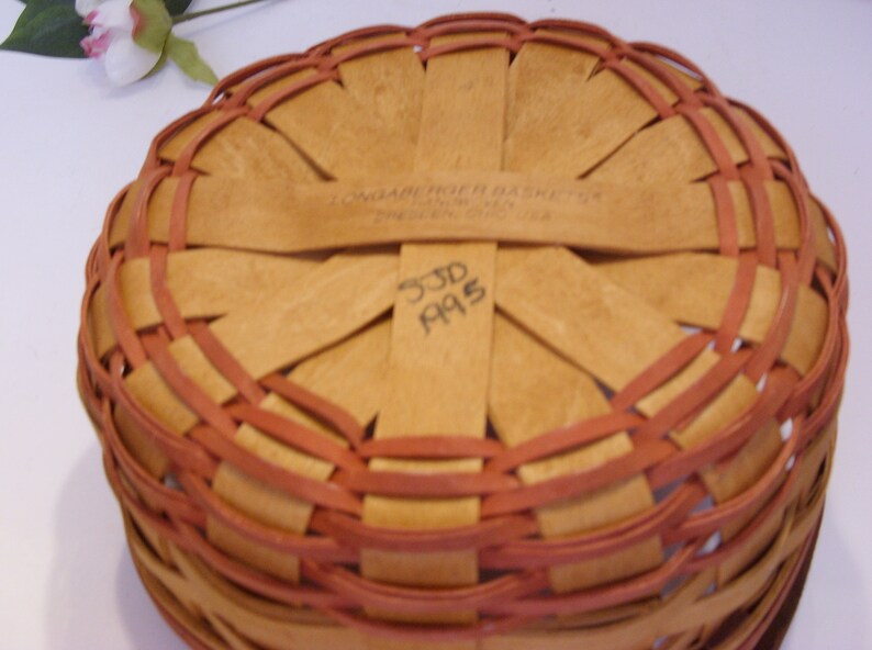 May include: A woven basket with a brown and red pattern. The bottom of the basket has a label that reads "Longaberger Basket Co.  744  330-672-1314" and the number "33D A95" is written in black marker.