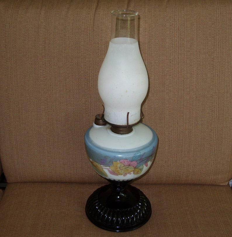 May include: A vintage oil lamp with a white frosted glass shade and a blue and white floral patterned base. The base has a black metal stand.