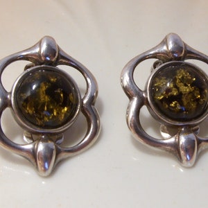 May include: A pair of silver earrings with green amber stones set in a floral design.
