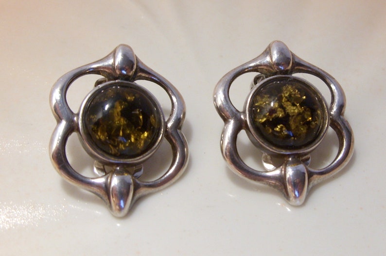 May include: A pair of silver earrings with green amber stones set in a floral design.