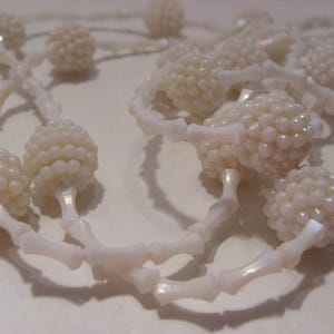 May include: A necklace featuring a series of white, textured, spherical beads alternating with smooth, elongated, bone-shaped spacers. The beads have a glossy, pearlescent finish, and the entire piece is constructed with a repeating pattern.