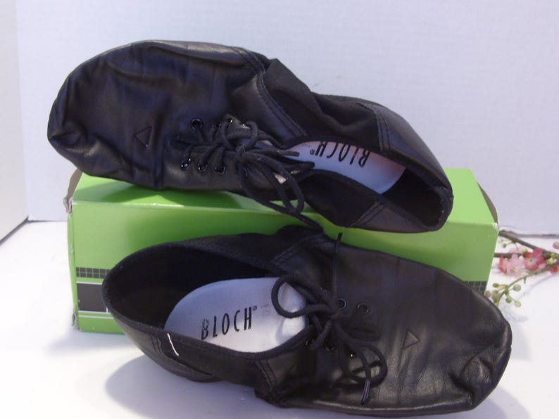 Puede incluir: Un par de zapatos de baile de cuero negro con cordones, apoyados en una caja verde. Los zapatos tienen un dise&ntilde;o suave y flexible y la marca "BLOCH" es visible en la plantilla. Zapatos de baile.