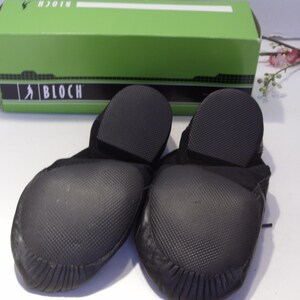 Puede incluir: Un par de zapatillas de baile negras con suelas texturizadas, frente a una caja verde con la marca "BLOCH". Los zapatos est&aacute;n hechos de un material suave y flexible, dise&ntilde;ado para bailar.