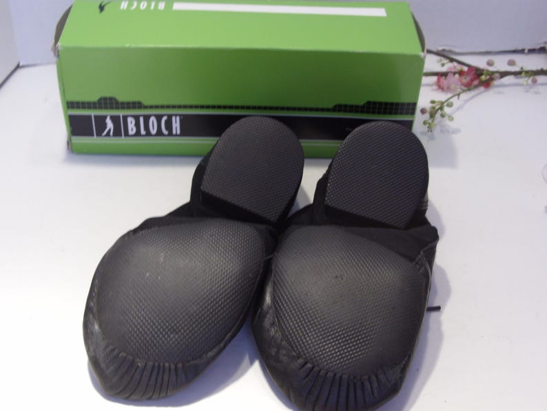 Puede incluir: Un par de zapatillas de baile negras con suelas texturizadas, frente a una caja verde con la marca "BLOCH". Los zapatos est&aacute;n hechos de un material suave y flexible, dise&ntilde;ado para bailar.