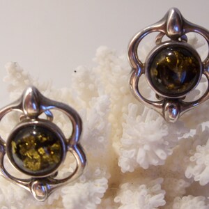 May include: A pair of silver earrings with a green amber stone in each. The earrings are in the shape of a flower with a round stone in the center.