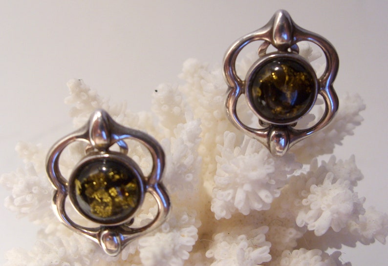 May include: A pair of silver earrings with a green amber stone in each. The earrings are in the shape of a flower with a round stone in the center.