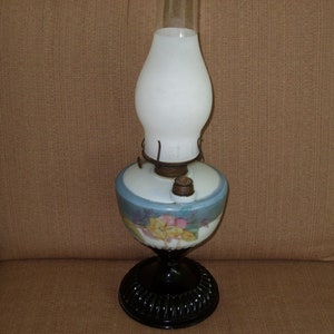 May include: A vintage oil lamp with a white glass shade and a blue and white floral patterned base. The base has a black metal stand.
