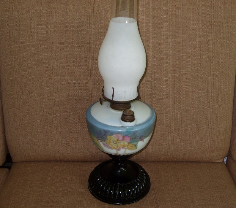 May include: A vintage oil lamp with a white glass shade and a blue and white floral patterned base. The base has a black metal stand.