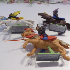 May include: Four plastic toy knights on horseback. The knights are wearing colorful armor and riding different colored horses. Each knight has a sword and shield. The horses are standing on green bases with the words "Fantastic Knights" printed on them.