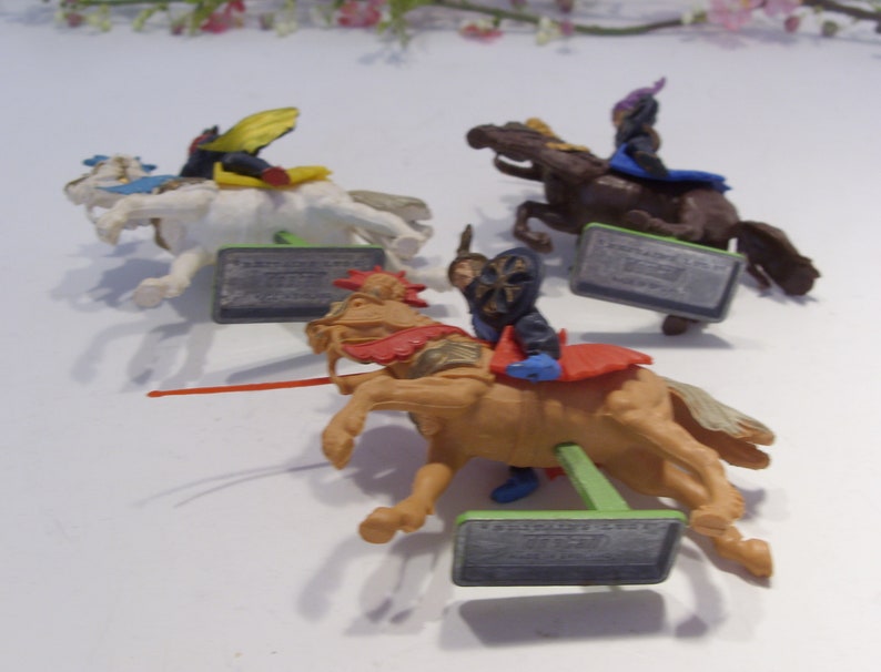 May include: Four plastic toy knights on horseback. The knights are wearing colorful armor and riding different colored horses. Each knight has a sword and shield. The horses are standing on green bases with the words "Fantastic Knights" printed on them.