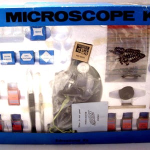 May include: A vintage microscope kit in a blue box, labeled "MICROSCOPE KIT" in white. The kit includes a microscope, slides, vials, and a butterfly specimen. The kit also includes a booklet and other accessories.