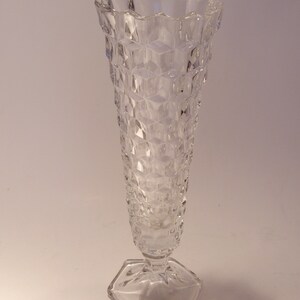 Puede incluir: Un jarr&oacute;n de cristal transparente con un patr&oacute;n de diamantes y una base hexagonal. El jarr&oacute;n tiene un borde acampanado y festoneado y un cuerpo largo y esbelto. El jarr&oacute;n mide unos 25 cm de alto.