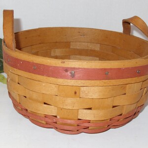 May include: A woven basket with two leather handles. The basket is made of natural wood and has a red trim around the top and bottom.