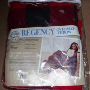 Op de afbeelding: Een rood en zwart geruite oversized deken in een doorzichtige plastic verpakking. De deken is gemaakt van 100% virgin acryl en meet 137 cm x 183 cm. De verpakking bevat de tekst "REGENCY OVERSIZE THROW".