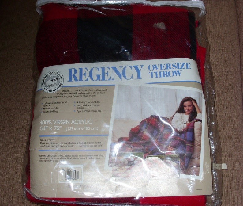 Op de afbeelding: Een rood en zwart geruite oversized deken in een doorzichtige plastic verpakking. De deken is gemaakt van 100% virgin acryl en meet 137 cm x 183 cm. De verpakking bevat de tekst "REGENCY OVERSIZE THROW".