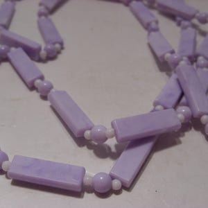 May include: A long necklace featuring a repeating pattern of light purple rectangular beads and smaller light purple spherical beads, separated by tiny white spacer beads. The rectangular beads have a marbled texture in shades of lavender.