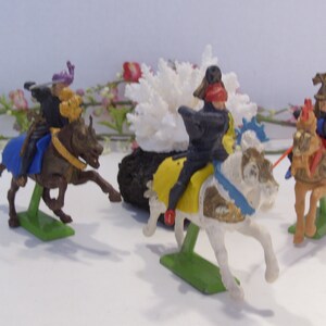 May include: Four plastic toy knights on horseback. The knights are wearing colorful armor and helmets. The horses are white, brown, and tan. The knights are posed in a battle scene.