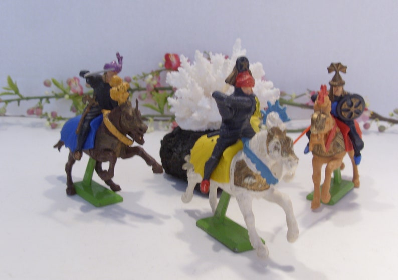 May include: Four plastic toy knights on horseback. The knights are wearing colorful armor and helmets. The horses are white, brown, and tan. The knights are posed in a battle scene.