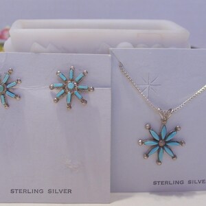 May include: A sterling silver necklace and earrings set with turquoise flower pendants. The necklace has a delicate chain and the earrings are stud style.