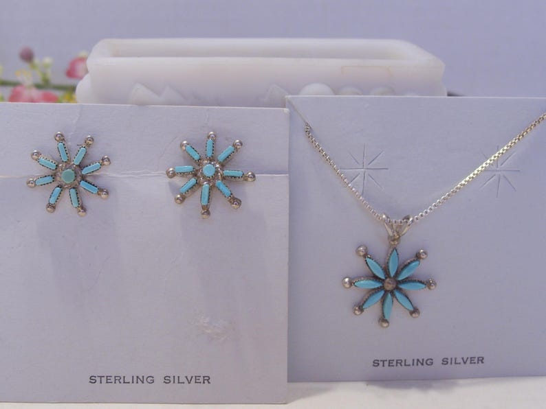 May include: A sterling silver necklace and earrings set with turquoise flower pendants. The necklace has a delicate chain and the earrings are stud style.
