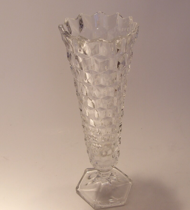 Puede incluir: Un jarr&oacute;n de vidrio transparente con base hexagonal y cuerpo texturizado con dise&ntilde;o de diamantes. El borde superior tiene un dise&ntilde;o festoneado. El jarr&oacute;n es alto y delgado, adecuado para exhibir flores o como pieza decorativa.