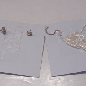 May include: A pair of silver earrings and a silver chain necklace on a white background.