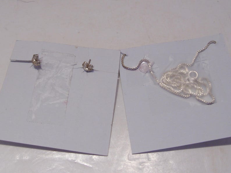 May include: A pair of silver earrings and a silver chain necklace on a white background.