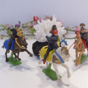 May include: Four plastic toy knights on horseback, each with a different colored horse and armor. The knights are posed in a battle scene, with swords drawn and shields raised. The horses are all in motion, with their legs raised in mid-stride.