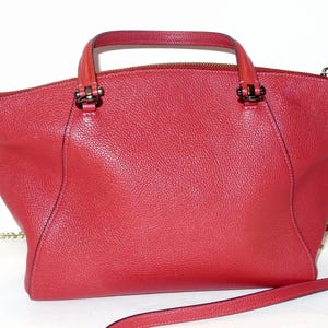 May include: A red leather handbag with a top handle and a detachable shoulder strap. The bag has a zip closure and dark metal hardware. The leather has a textured grain.