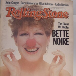 May include: A magazine cover featuring Bette Midler with a red clown nose, smiling and holding her hands up to her face. The magazine is Rolling Stone and the headline reads "The Divine Ms. Midler Bette Noire".