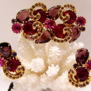 May include: A set of vintage earrings and a brooch featuring a swirl design with purple, pink, and gold accents.