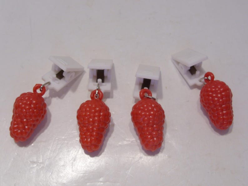 Op de afbeelding: Vier rode aardbeivormige bedels met witte clips. De bedels hebben een gestructureerd oppervlak en zijn met kleine zilveren ringen aan de clips bevestigd. De clips zijn wit en hebben een zwarte metalen veer.