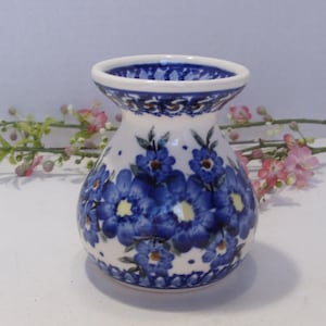May include: A white ceramic vase with a flared top and a rounded body. The vase is decorated with blue floral patterns and a blue rim. The flowers have yellow centers. The vase is approximately 5 inches tall.