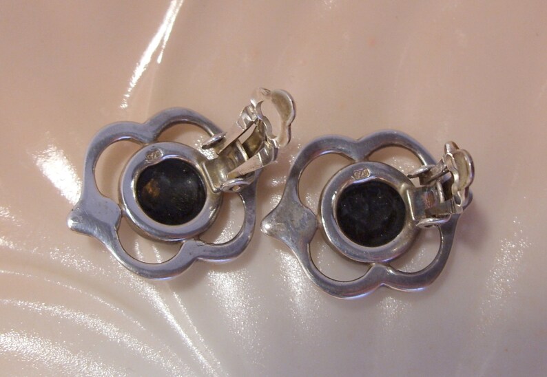May include: A pair of silver clip-on earrings with a floral design and black stones in the center.