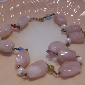 May include: A delicate bracelet featuring large, faceted rose quartz beads, interspersed with small white pearls and colorful accent beads. The bracelet is strung on a gold-toned chain and has a secure clasp.