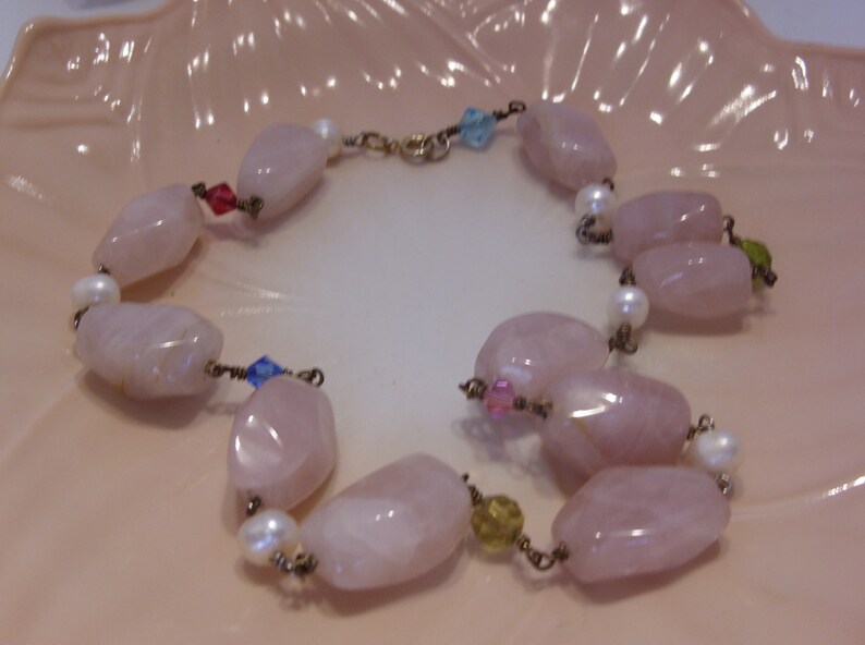 May include: A delicate bracelet featuring large, faceted rose quartz beads, interspersed with small white pearls and colorful accent beads. The bracelet is strung on a gold-toned chain and has a secure clasp.