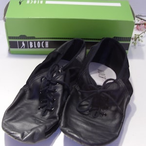 Puede incluir: Zapatos de baile de cuero negro con cordones, frente a una caja verde con el logo de Bloch. Los zapatos tienen un dise&ntilde;o suave y flexible, adecuado para varios estilos de baile. La caja est&aacute; en el fondo.