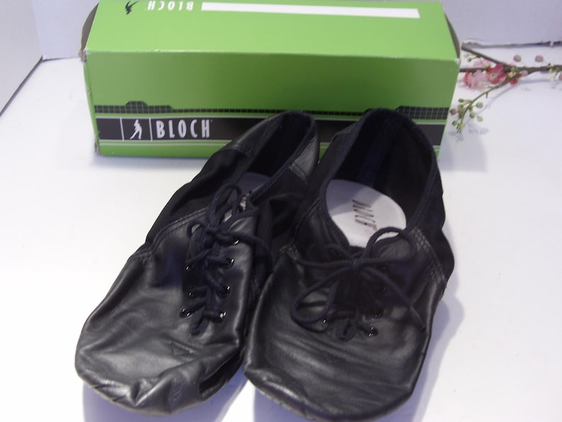 Puede incluir: Zapatos de baile de cuero negro con cordones, frente a una caja verde con el logo de Bloch. Los zapatos tienen un dise&ntilde;o suave y flexible, adecuado para varios estilos de baile. La caja est&aacute; en el fondo.