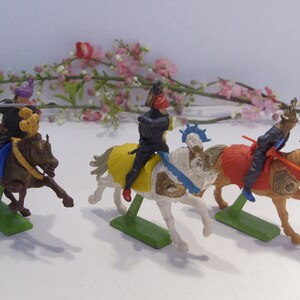 May include: Three plastic toy knights on horseback, each with a different colored horse and armor. The knights are holding swords and lances. The horses are in a running pose.