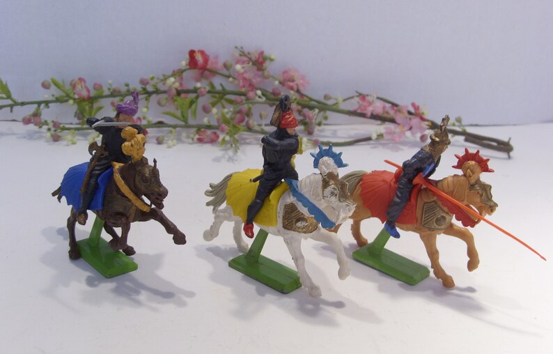 May include: Three plastic toy knights on horseback, each with a different colored horse and armor. The knights are holding swords and lances. The horses are in a running pose.