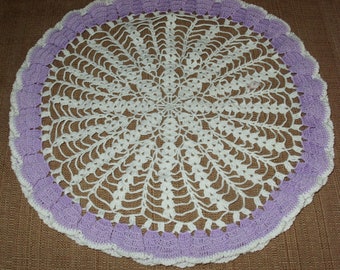 May include: A white crocheted doily with a purple crocheted border. The doily is circular and has a delicate, lacy design.