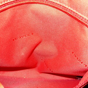 May include: Close-up of the interior of a red Coach handbag. The fabric is a solid red with a subtle texture. The word "COACH" is visible in the center of the image. A red zipper is visible along the top edge.