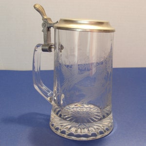 May include: Clear glass beer stein with a metal hinged lid and handle. The glass is etched with a design of birds and foliage. The base of the stein has a decorative, scalloped design.