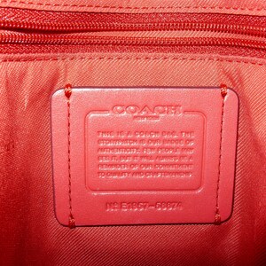 May include: Close-up of the interior of a red Coach bag. The image shows a red leather tag with the Coach logo and text, stitched onto the red fabric lining. A red zipper is visible at the top of the image.