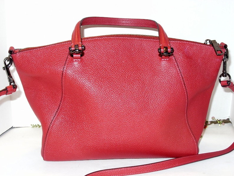 May include: A red leather handbag with a top handle and a detachable shoulder strap. The bag has a textured surface, a zipper closure, and dark metal hardware. The bag's design is a classic, structured style.